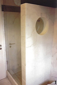 Gemauerte Duschabtrennung aus den 50iger Jahren, durch ein rundes Fenster optisch aufgelockert und mit Marmor verkleidet