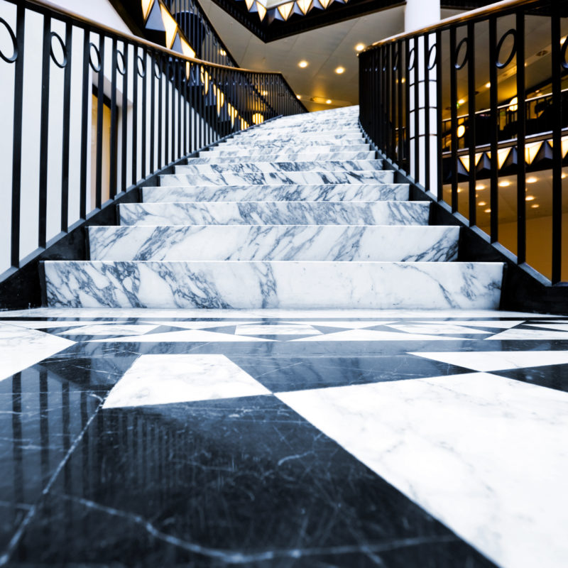 Helle Marmortreppe mit dunkler Maserung und schwarz-weißem Marmorboden.