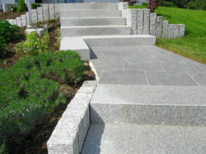 Treppe durch den Garten aus massiven grauen Granitstufen samt Plattenbelag auf dem Weg und Beetbegrenzung