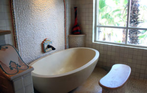 Edle Badewanne, umrahmt von einem beigen Kalksteinfußboden, weißen Kieseln als Wandbelag und Mosaikverzierungen